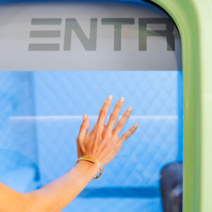 A close-up of a female patient's hand pushing open the door to SUMA Life House's custom hyperbaric chamber, used for hyperbaric chamber treatment in Greenwich, CT.