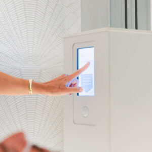 A female SUMA Life House specialist, wearing a gold bracelet, adjust the setting of the Ammortal Chamber. This red light treatment near Westport, CT, combines 4 advanced therapies for a premium wellness experience.