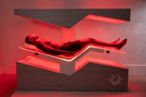 A male SUMA Life House guests, wearing black shorts, relaxes under the red glow of the Ammortal Chamber. The best red light bed treatment in Greenwich, CT, the Chamber features a